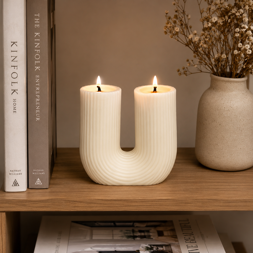 A U-shaped ceramic candle holder with two lit candles, styled on a wooden shelf next to books and a vase of dried flowers.
شمعة قوس مزدوجة كريمي بتصميم مخطط وفتيلين، مناسبة لديكور الكونسول والأرفف وتنسيقات المنزل المودرن.
