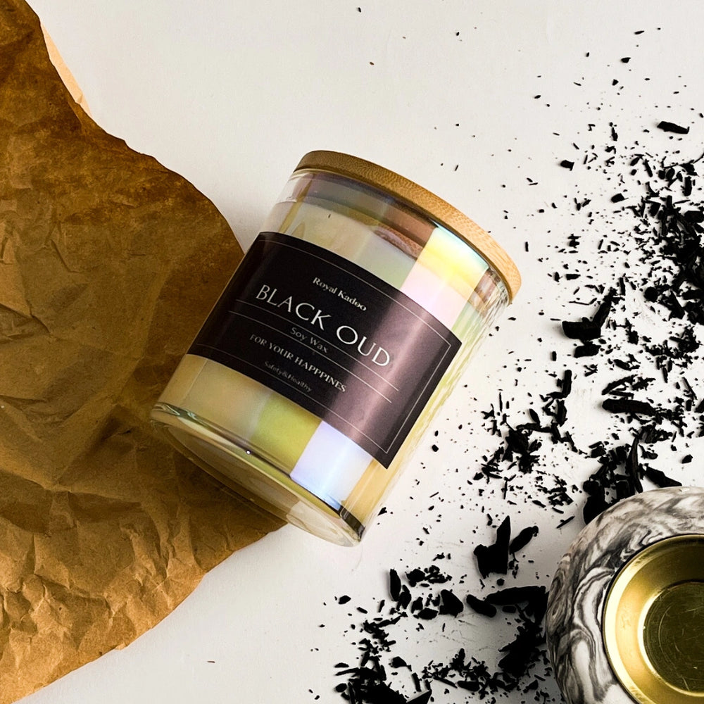 Candle labeled 'Black Oud' with tea leaves on a textured surface
شمعة بلاك عود معطرة من شمع الصويا داخل عبوة زجاجية أنيقة بغطاء خشبي وملصق أسود، بتصميم فاخر مناسب لتعطير وديكور المنزل.