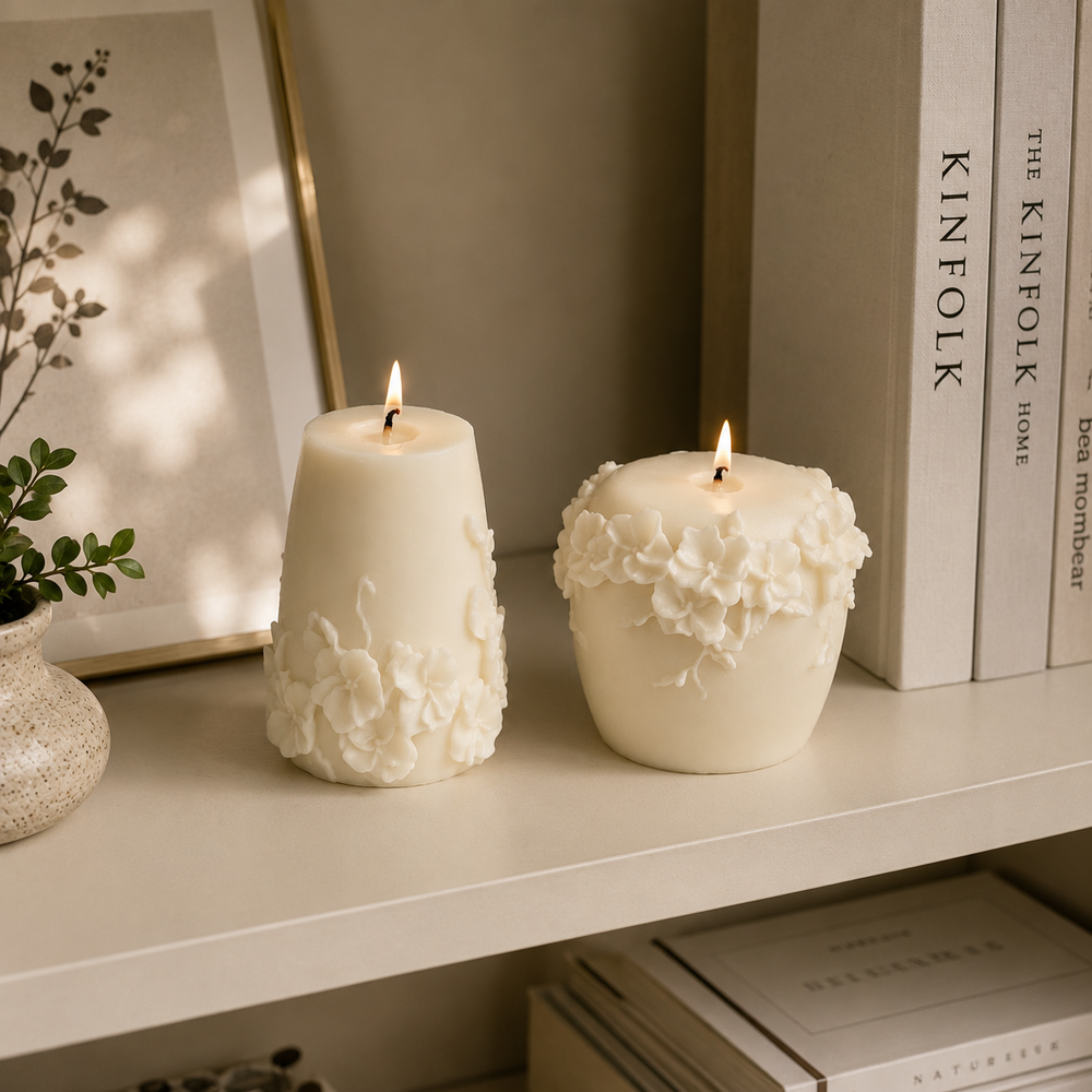 Two lit cream-colored candles with 3D floral sculpted details, displayed on a white shelf next to books and a small potted plant.
طقم شمعتين كريمي بتصميم زهور بارزة ثلاثية الأبعاد بأشكال مختلفة، مناسب لديكور الكونسول والأرفف وطاولة القهوة.