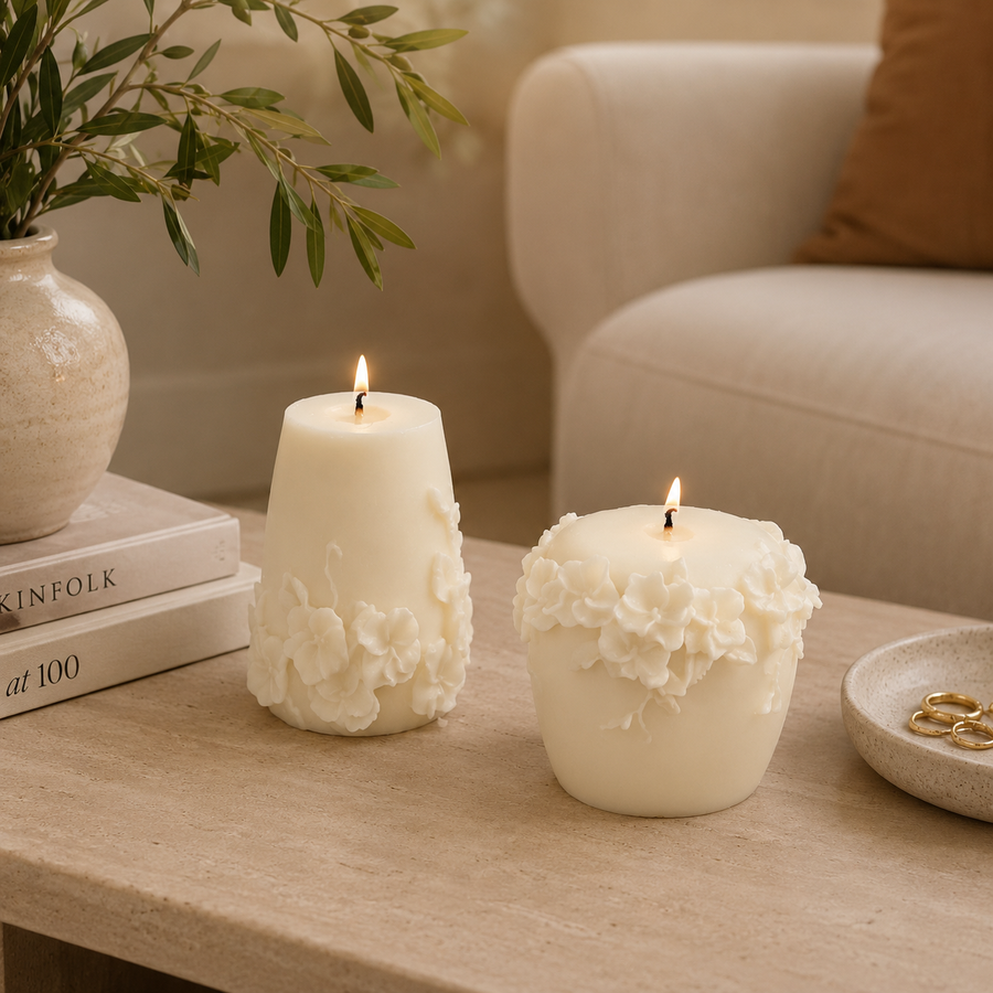 Two lit cream-colored wax candles with 3D floral sculpted details, displayed on a light stone table in a cozy living room setting.
طقم شمعتين كريمي بتصميم زهور بارزة ثلاثية الأبعاد بأشكال مختلفة، مناسب لديكور الكونسول والأرفف وطاولة القهوة.