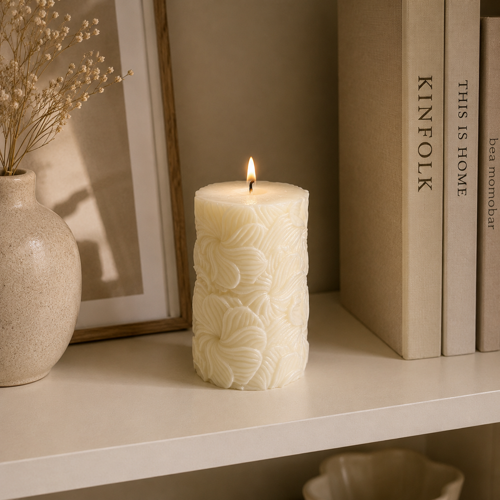A lit cream-colored pillar candle with an embossed floral pattern sits on a white shelf next to books and a vase with dried flowers.
شمعة ديكور كريمي أسطوانية مزينة بتفاصيل أوراق شجر بارزة، مناسبة للكونسول وطاولة القهوة وديكور المنزل المودرن.
