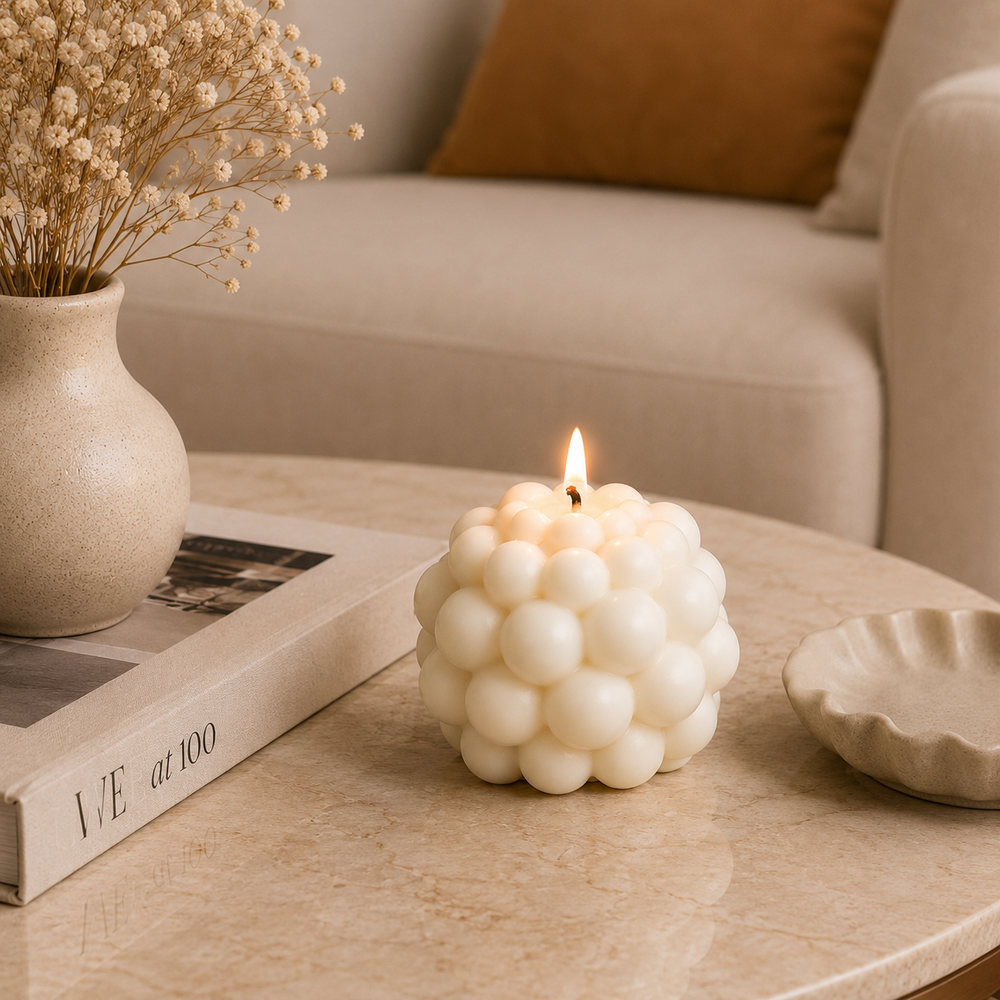 A lit white cluster candle sits on a round beige marble table in a softly styled living room setting, with a vase of dried flowers, a book, and a small dish nearby.
شمعة بابل كريمي بتصميم فقاعات ثلاثية الأبعاد مودرن لتزيين طاولة القهوة والكونسول وديكور المنزل.