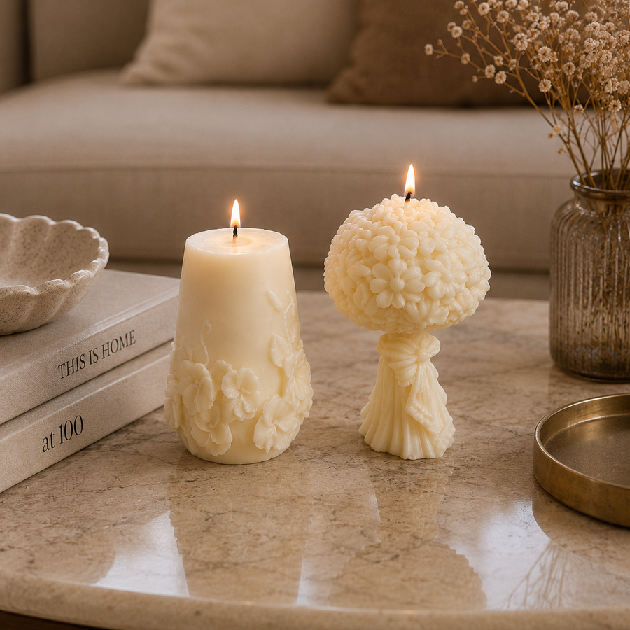 Two cream-colored decorative candles lit on a polished stone table in a cozy living room setting. One candle has a flared base with embossed floral details, and the other has a textured, bulbous top resembling a bouquet.
طقم شموع ديكور ورد كريمي من قطعتين بتصميم زهور بارزة وباقة ورد لتزيين الكونسول والأرفف.
