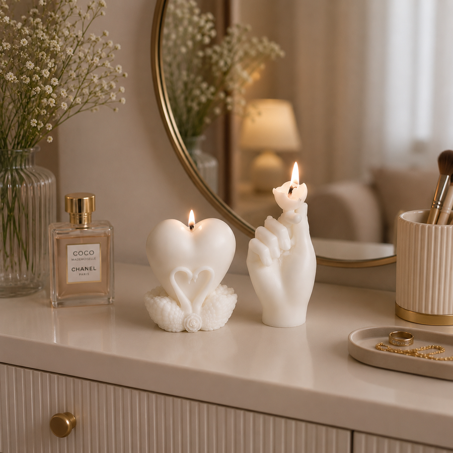 Two white sculptural candles on a vanity table, one shaped like a heart with a flame and one shaped like a hand holding a flower, styled in a warm, softly lit room with a Chanel perfume bottle and a round mirror in the background.
طقم شموع ديكور كريمي بتصميم قلب ويد رومانسية، منسق على طاولة خشبية داخل غرفة معيشة بديكور هادئ ومودرن.