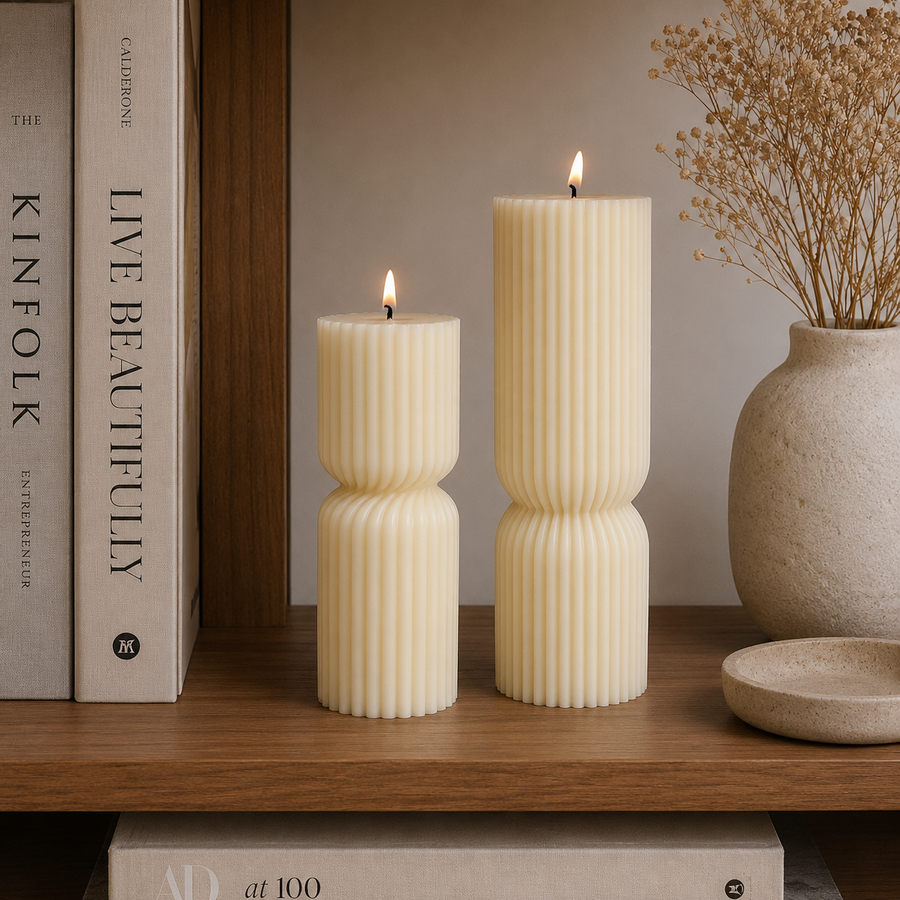 Two cream-colored ribbed pillar candles, one short and one tall, lit and standing on a wooden shelf next to books and a ceramic vase with dried flowers.
طقم شموع ديكور مودرن كريمي مكون من شمعتين مخططتين بأحجام مختلفة وتصميم هندسي أنيق للكونسول والأرفف.