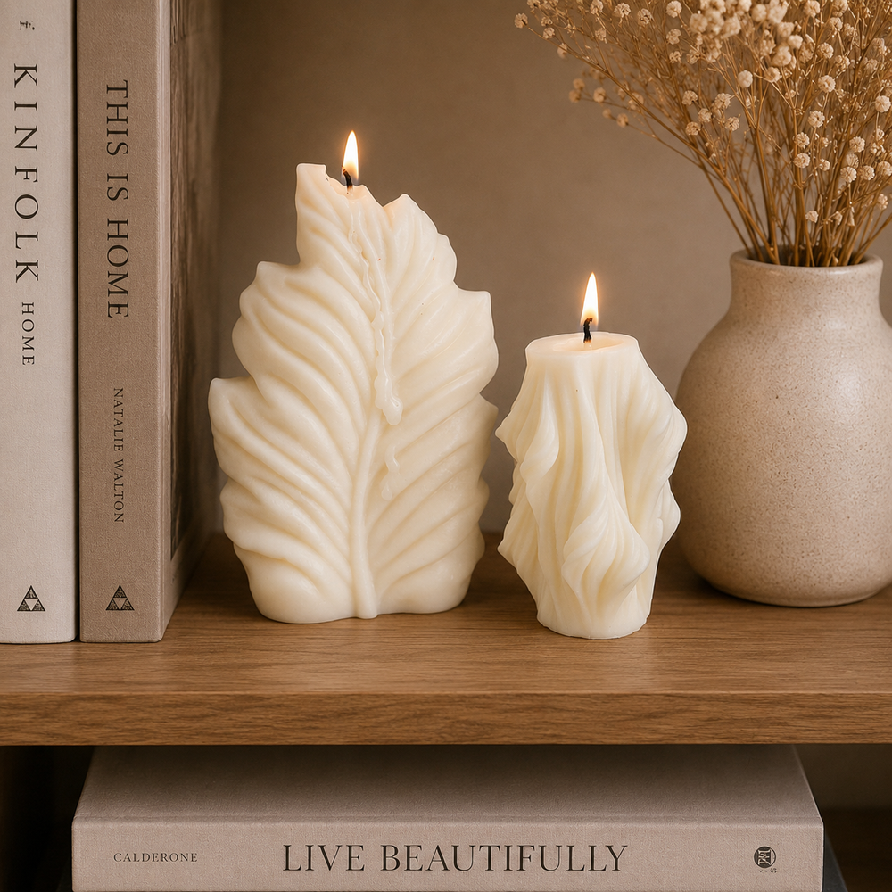 Two cream-colored leaf-shaped pillar candles with lit flames sit on a wooden shelf next to books and a ceramic vase with dried flowers.
طقم شموع ديكور أوراق الشجر كريمي من قطعتين بأحجام مختلفة وتصميم منحوت مستوحى من الطبيعة للكونسول والأرفف.