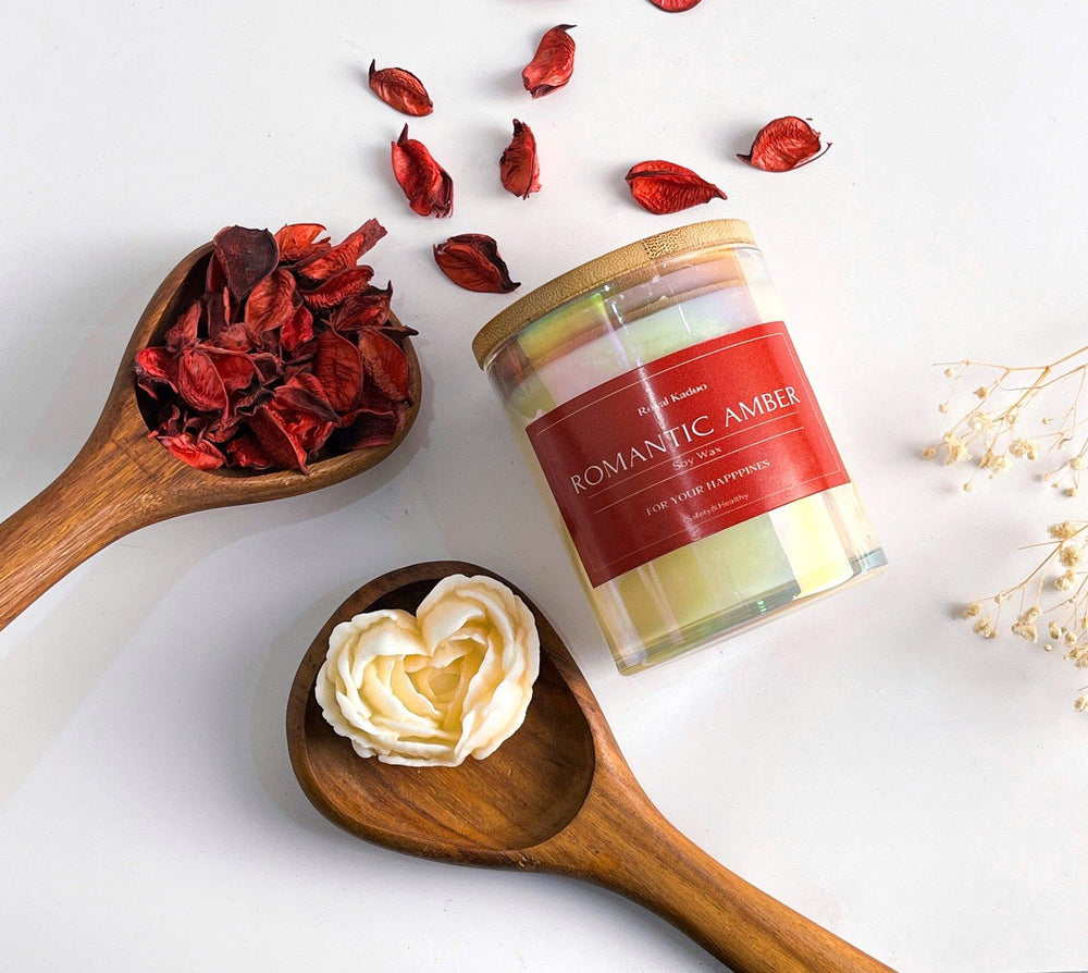 Candle jar labeled 'Romantic Amber' with wooden spoons containing dried flowers and cream on a light background.
شمعة رومانتك أمبر معطرة من شمع الصويا داخل عبوة زجاجية بغطاء خشبي، منسقة بجوار بتلات زهور حمراء وديكور خشبي أنيق.