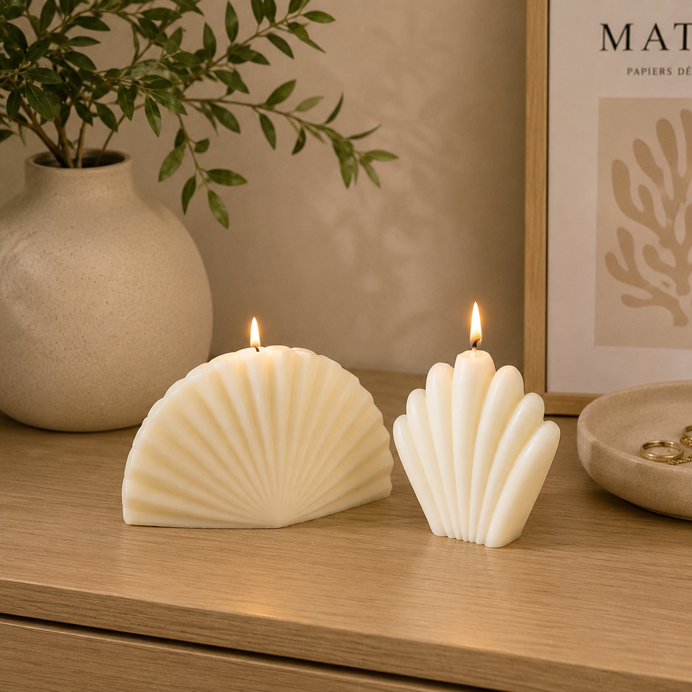 Two white shell-shaped candles with lit flames sit on a wooden table, styled with a beige ceramic vase containing green leaves and a framed print in the background.
طقم شموع ديكور كريمي مكون من شمعتين بتصميم صدف بحري عصري، مناسب لديكور الكونسول وطاولة القهوة والمنزل المودرن.
