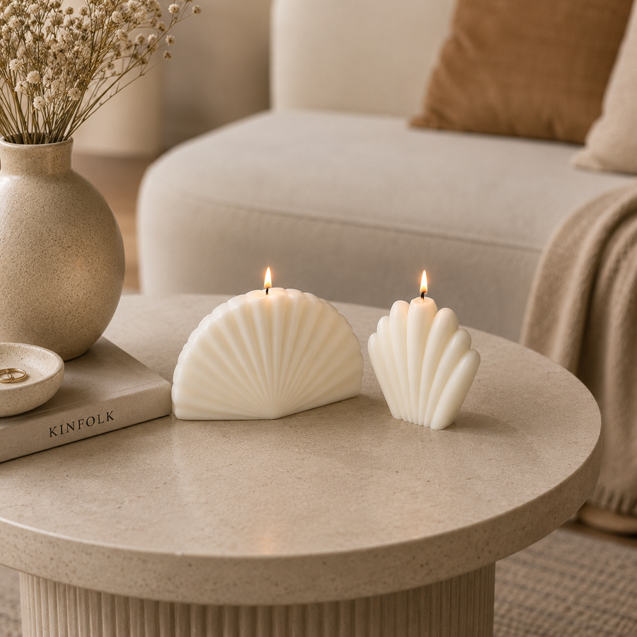 Two white seashell-shaped candles are lit on a round beige stone table in a cozy living room setting, with a vase of dried flowers and a book nearby.
طقم شموع ديكور كريمي مكون من شمعتين بتصميم صدف بحري عصري، مناسب لديكور الكونسول وطاولة القهوة والمنزل المودرن.