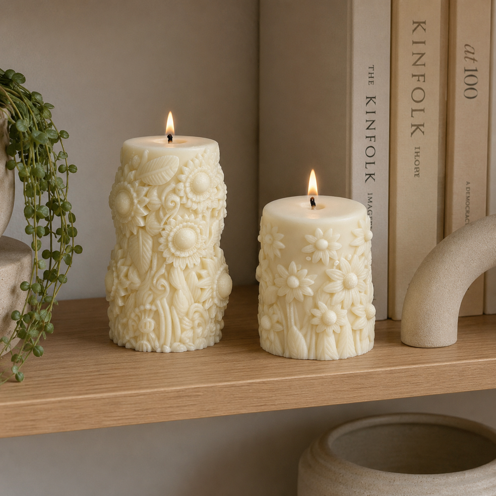 Two cream-colored, hand-carved pillar candles with lit flames sit on a light wood shelf next to books and a plant.
طقم شمعتين كريمي بتصميم زهور بارزة ثلاثية الأبعاد بأحجام مختلفة، مناسب لديكور الكونسول والأرفف وطاولة القهوة.