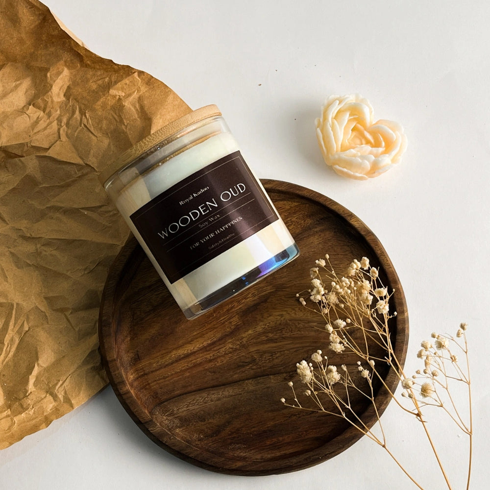 Candle labeled 'Wooden Oud' on a wooden tray with decorative elements on a light background
شمعة العود الخشبي المعطرة من شمع الصويا داخل عبوة زجاجية أنيقة بغطاء خشبي، موضوعة على صينية خشبية بجوار زهور مجففة.