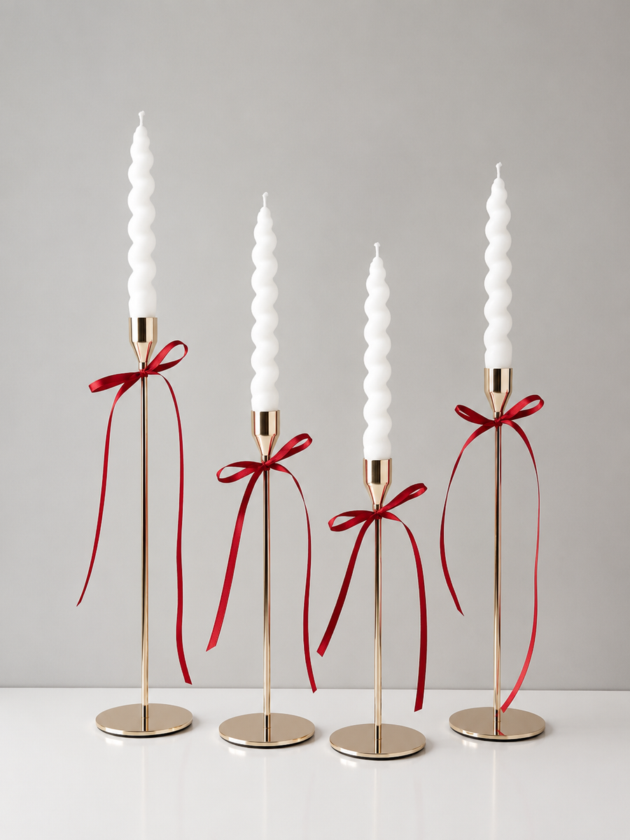 Set of four white twisted taper candles tied with a white satin ribbon, displayed on a textured beige fabric background for elegant home décor and gift presentation.