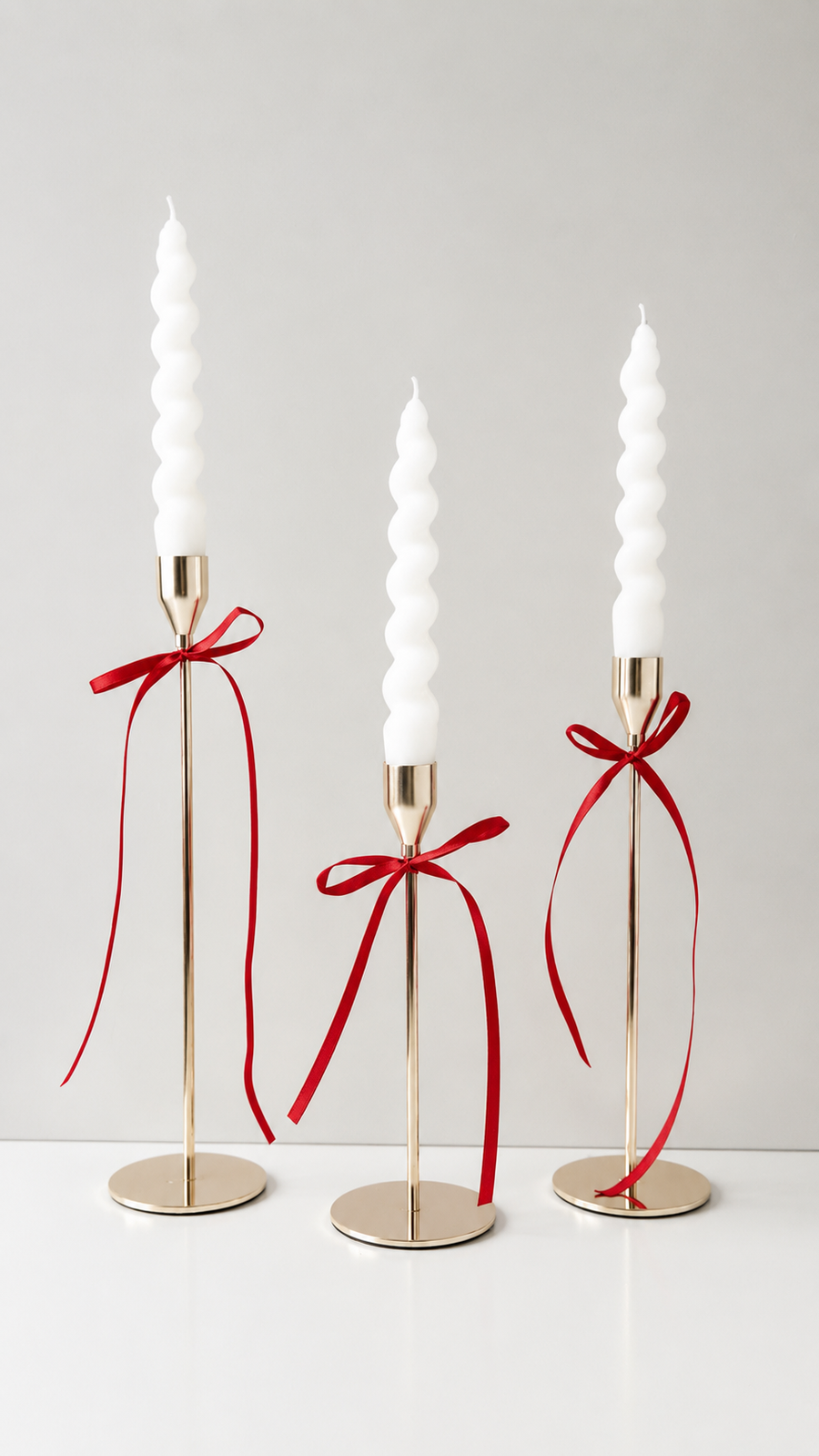 Set of white twisted taper candles tied with a cream satin ribbon, displayed on a golden candlesticks holder.
