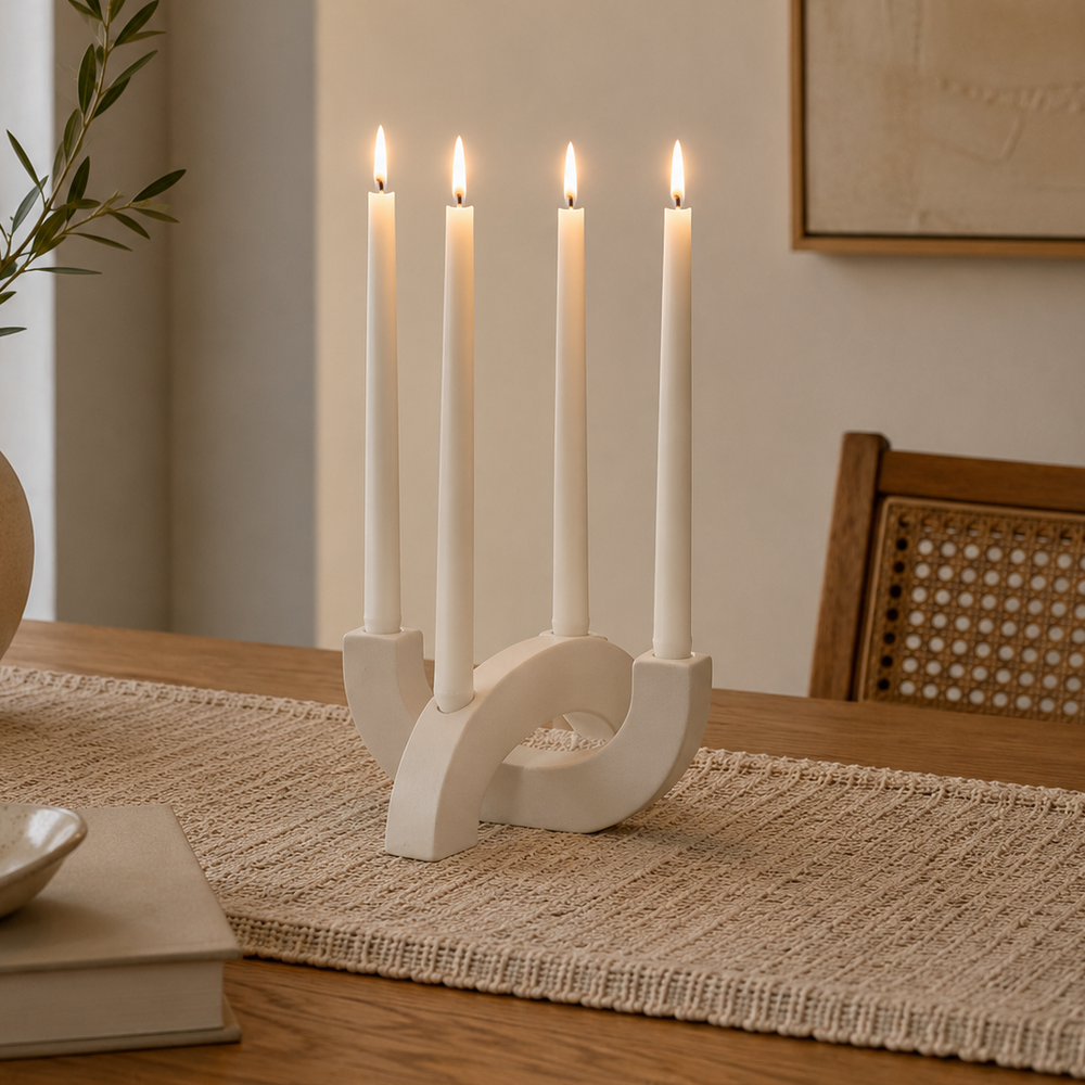White four-arm sculptural candlestick holder with four matching white taper candles, styled on a woven table runner in a modern dining room for elegant home décor.